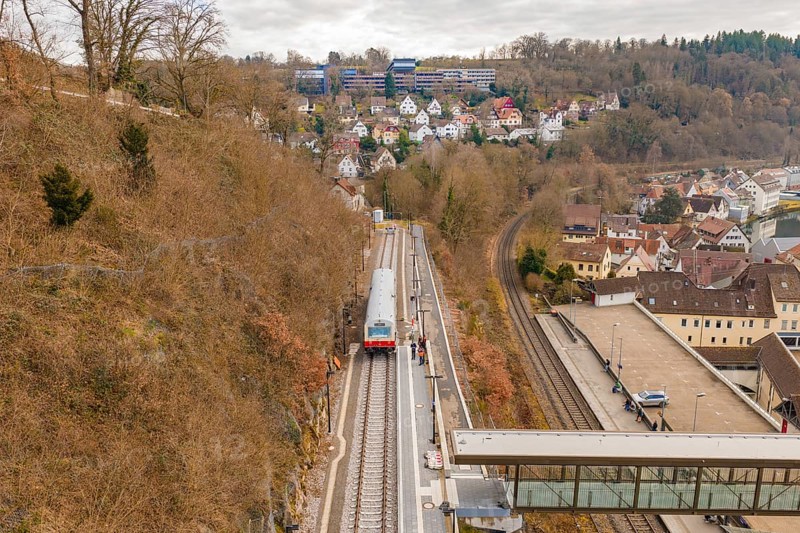 A train travels through a hilly urban landscape with wooded slopes and isolated houses under cloudy skies, historical event, first test run with a passenger train on the Hermann tracks, Hesse Railway since 1988, Calw, Calw district, Germany