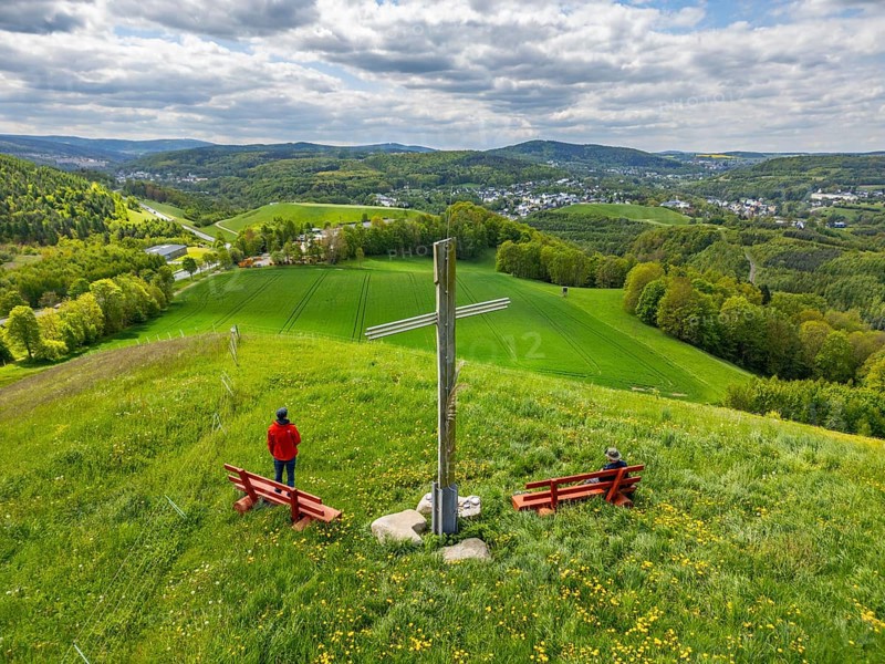 Two hikers under the Silberberg Pilgrim Cross with views over green landscapes, Bad Schlema, Ore Mountains, Saxony, Germany