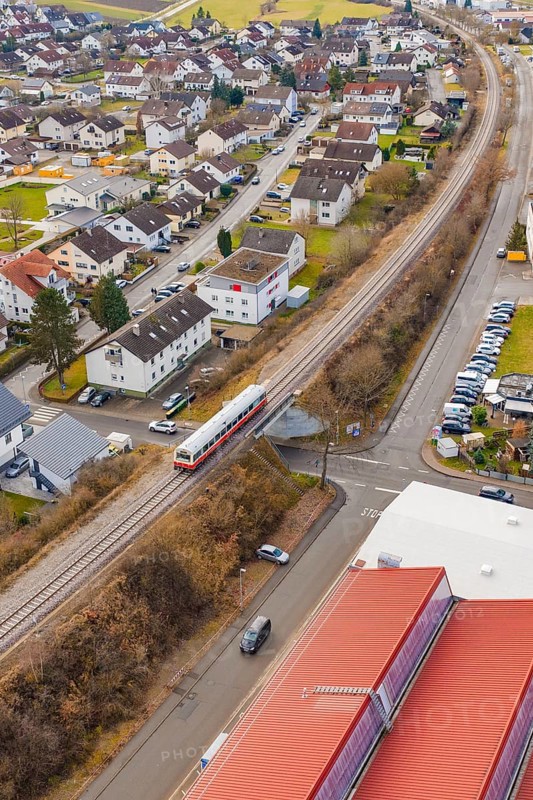 Train crossing a road junction in a residential and industrial area with red roofs, historic event, first test drive with a passenger train on the Hermann tracks, Hesse Railway since 1988, Althengstett, Calw district, Germany