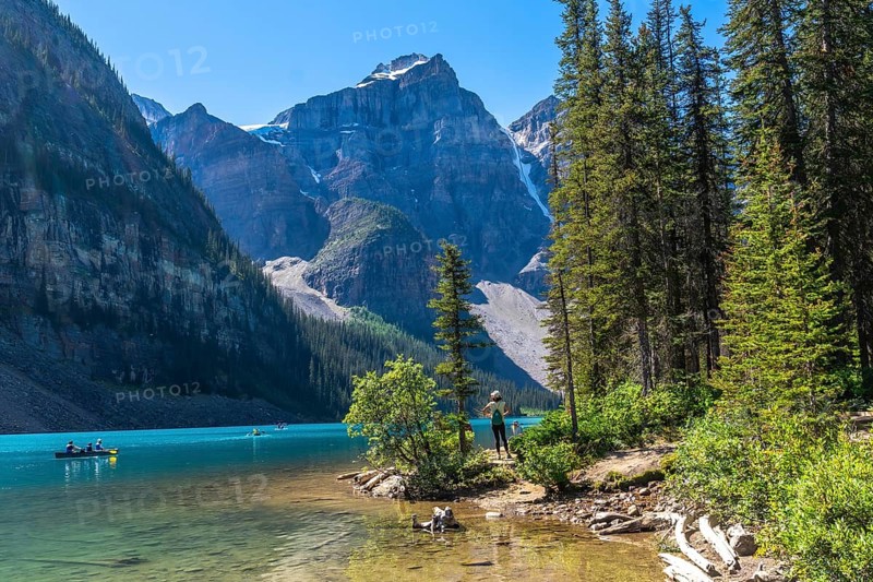 Tourists are canoeing on the turquoise, glacier fed moraine lake with its surrounding mountains and lush vegetation in banff national park, alberta, canada, during a sunny day