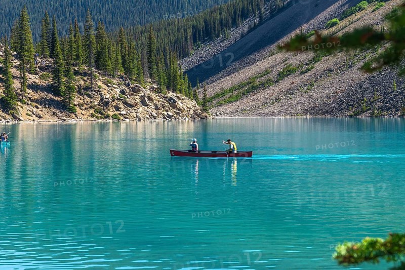 Two tourists paddling a red canoe on the turquoise waters of moraine lake in banff national park, surrounded by the breathtaking canadian rockies and lush pine trees