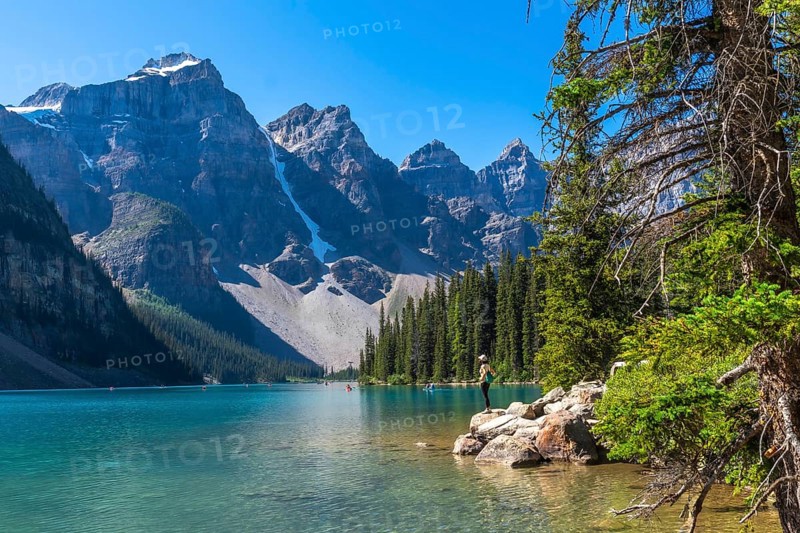 Moraine lake in banff national park displays its turquoise waters, surrounded by majestic mountains and lush vegetation, while a tourist admires the breathtaking landscape