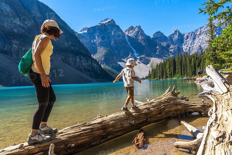 Mother and son balancing on a weathered log over turquoise waters of moraine lake, surrounded by the stunning canadian rockies in banff national park, enjoying a family adventure