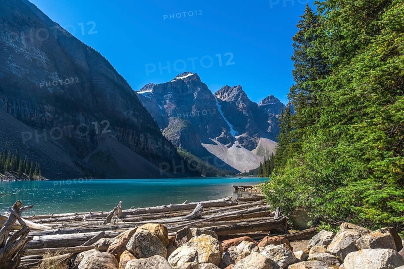 Driftwood logs and rocks resting on the shore of moraine lake, featuring stunning turquoise water and the majestic canadian rockies in banff national park