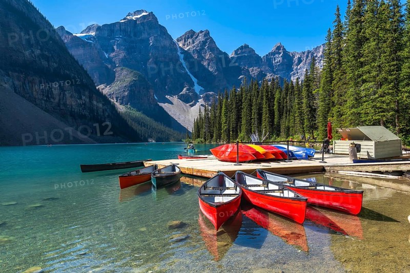 Reflecting red canoes in the turquoise waters of moraine lake, framed by snow capped mountains and pine trees, create a stunning landscape in banff national park, alberta