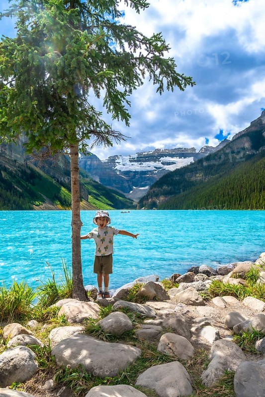 Young tourist with arms outstretched, enjoying the stunning turquoise waters of lake louise and the majestic canadian rockies in banff national park on a summer day