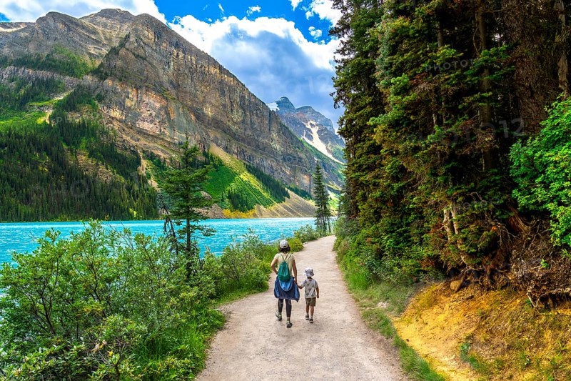 Mother and son walking along the scenic turquoise waters of lake louise with surrounding mountain peaks and lush green forest in banff national park, canadian rockies, alberta, canada