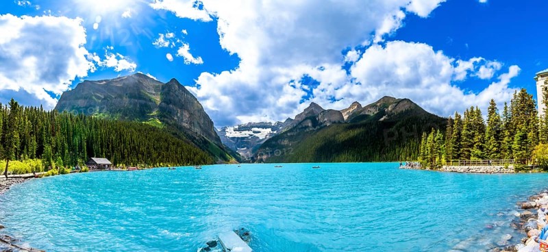 Panoramic view of tourists canoeing on turquoise lake louise, featuring the iconic fairmont chateau hotel amid mountains and pine trees in banff national park