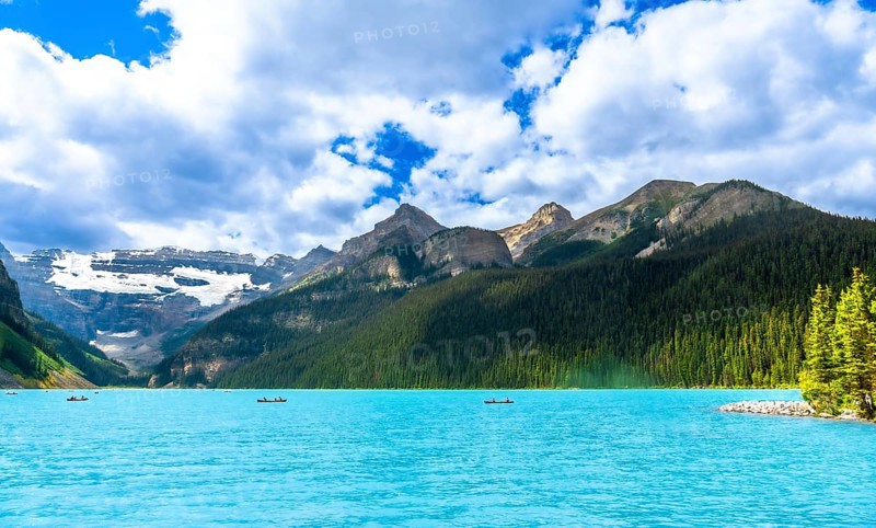 Canoeing on the turquoise waters of lake louise, tourists enjoy a breathtaking summer landscape framed by snow capped mountains and lush green forests in banff national park