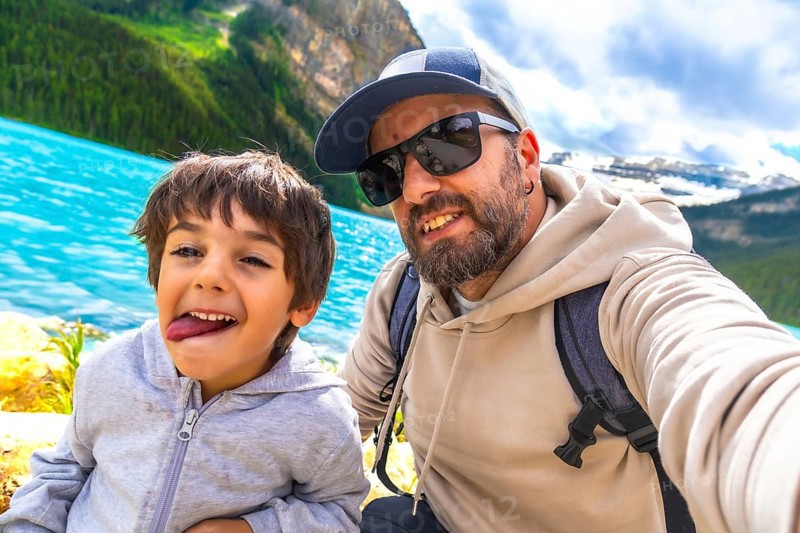 Father and son capturing a selfie by the turquoise waters of lake louise, surrounded by stunning mountain views during a memorable vacation in banff national park