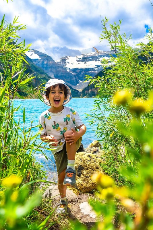 Young child having fun by the turquoise waters of lake louise with the majestic rocky mountains in the background, enjoying a sunny summer day in banff national park, alberta, canada