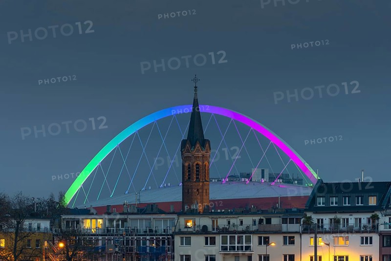 Evening view of residential buildings on the banks of the Rhine, behind them the church tower of St. John's Church and the rainbow illuminated arch of the Lanxess Arena, Cologne-Deutz, Cologne, North Rhine-Westphalia, Germany