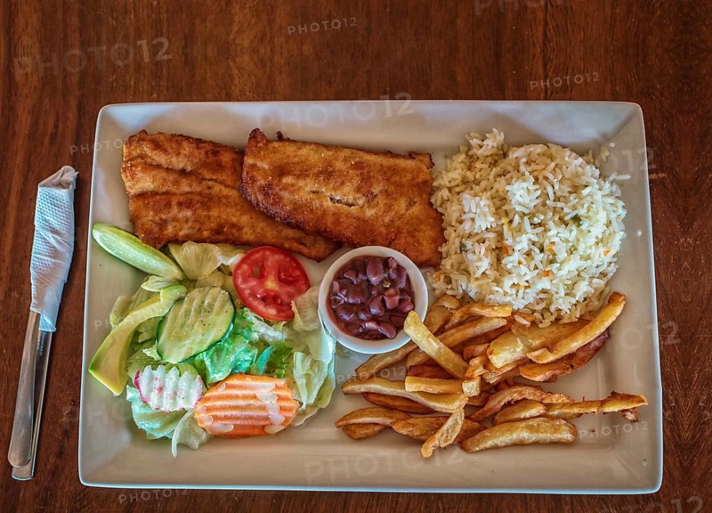 Plate of fried fish fillet with salad and french fries on wooden table, Top view of delicious fried fish fillet with french fries, rice and salad served on wooden table. Gourmet food plate
