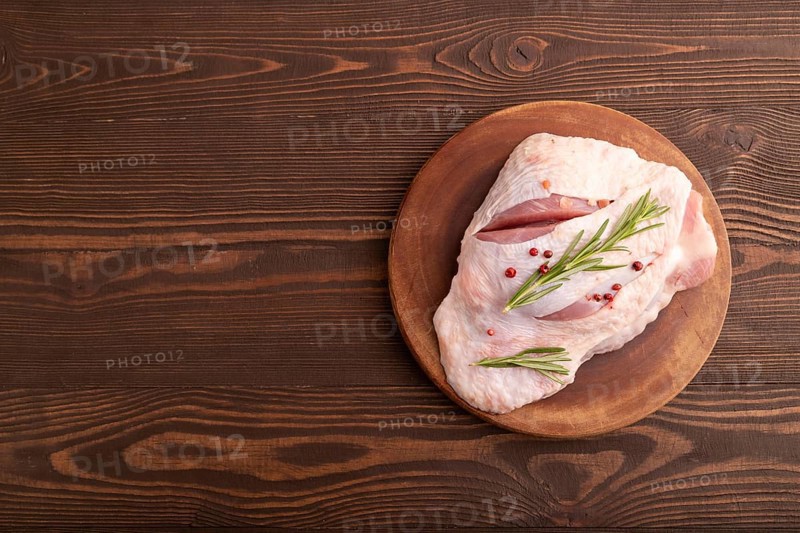 Raw Turkey Thigh with spices and rosemary on cutting board on brown wooden background. top view, flat lay, copy space