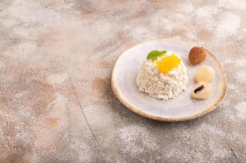 White ?ottage cheese, Curd, with orange and lychee on brown concrete background, side view, copy space