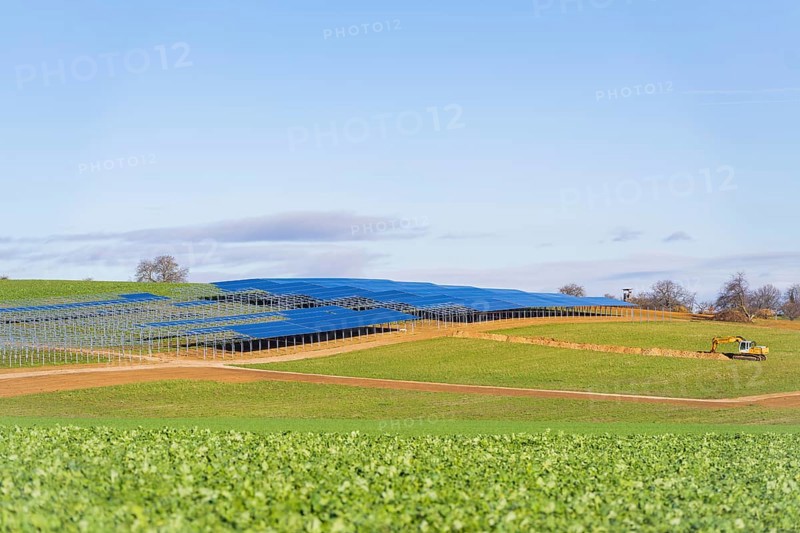 A tractor works in a field with installed solar panels under a blue sky, Energiewende, construction of PV open space, Baden-Württemberg, Germany
