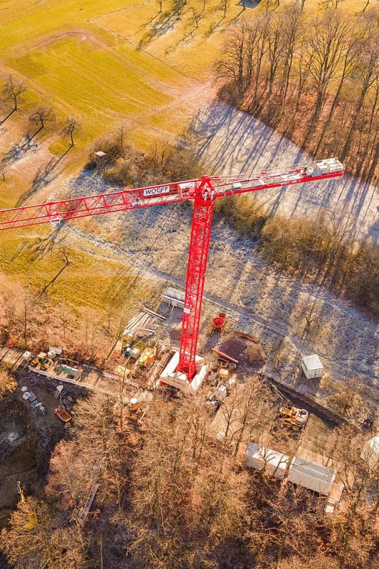 Red crane seen from the air on a construction site on the edge of a forest in an autumn landscape, construction of the Hermann Hesse Railway, Calw, Germany