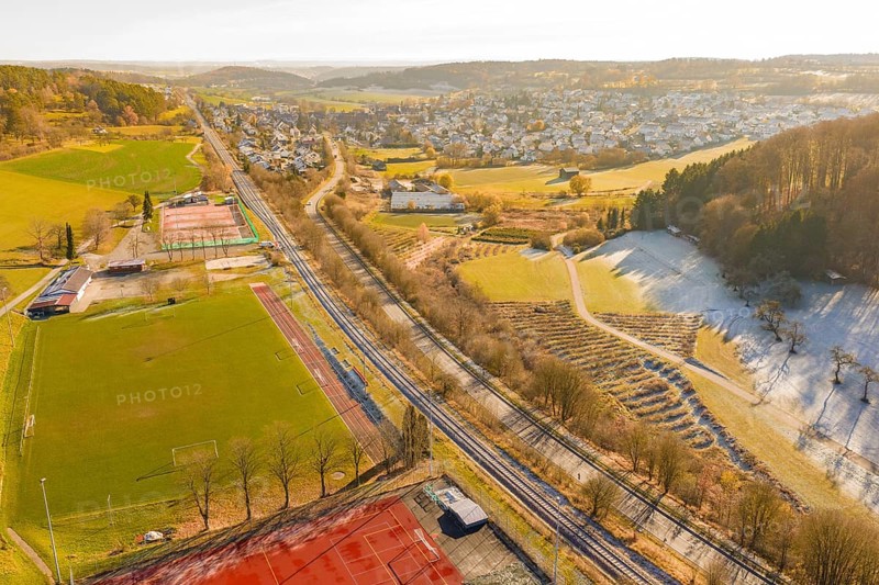 A railway traverses a scenic winter landscape with fields and a nearby village, construction of the Hermann Hesse Railway, Calw, Germany