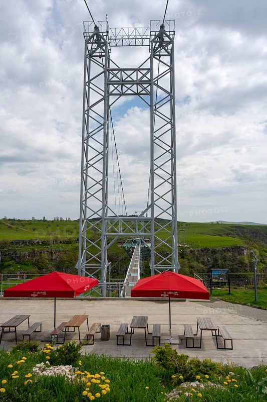 A tall metal structure with seating and red umbrellas in the foreground of nature, Diamond Bridge, Diamond Glass Bridge, world's longest free-hanging structure, Dashbashi Gorge, Khrami River, Chram, Tsalka Nature Reserve, Kartli, Georgia