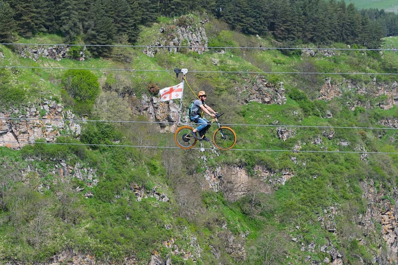 Person riding a bicycle on a rope in front of a wooded rocky landscape in the mountains, Dashbashi Gorge, Khrami River, Tsalka Nature Reserve, Kartli, Georgia