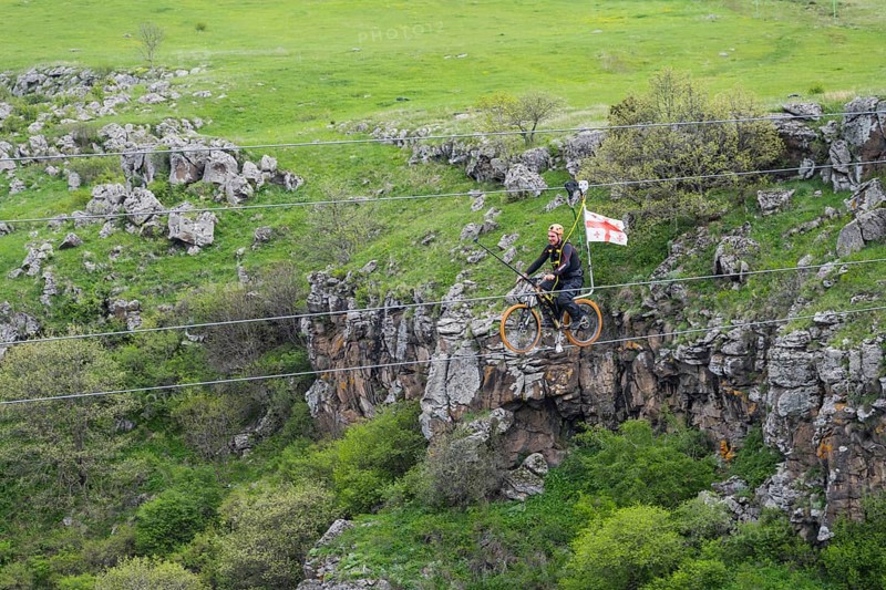 Person riding a bicycle on a stretched rope across a gorge in green countryside, Dashbashi Gorge, Khrami River, Tsalka Nature Reserve, Kartli, Georgia