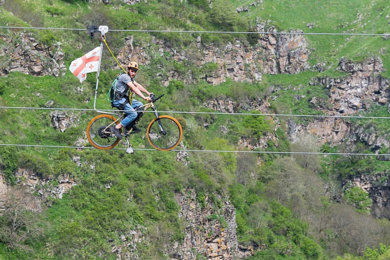 Man on a bicycle balancing at lofty heights above a green valley, Dashbashi Gorge, Khrami River, Tsalka Nature Reserve, Kartli, Georgia