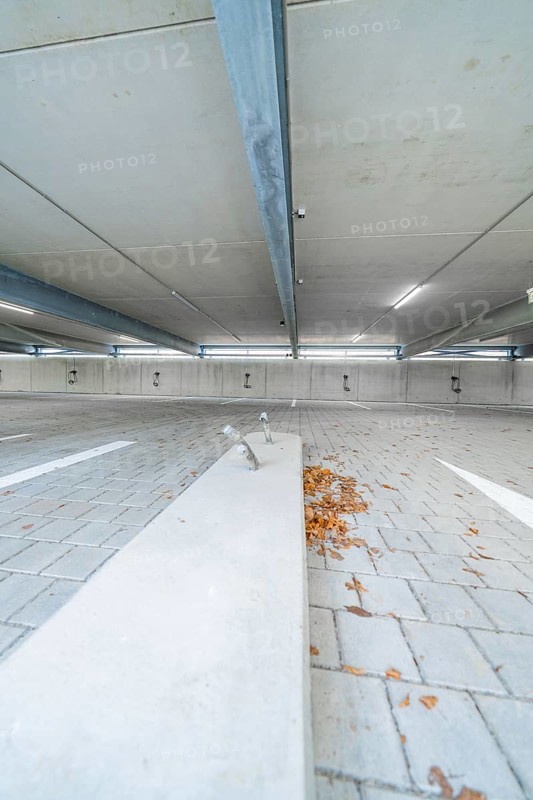 Empty parking lot with concrete floor, scattered leaves and parking space markings, parking garage construction with charging infrastructure, Calw, Germany