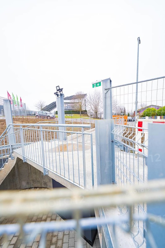Modern outdoor area with steel railings and flags, building complex in the background, parking garage construction with charging infrastructure, Calw, Germany