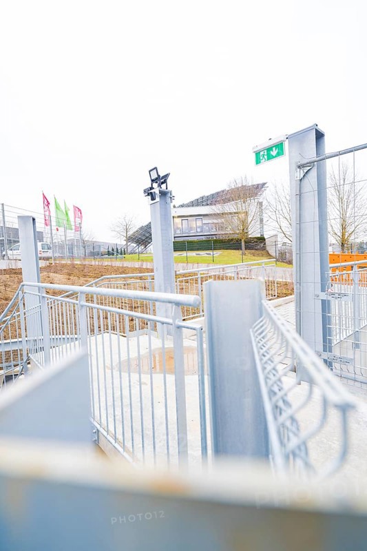 Entrance area with modern steel structure and flags, buildings in the distance, parking garage construction with charging infrastructure, Calw, Germany