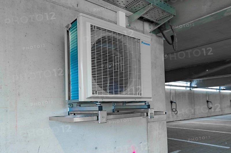 Air conditioner installed on an industrial bracket on a concrete wall indoors, parking garage construction with charging infrastructure, Calw, Germany