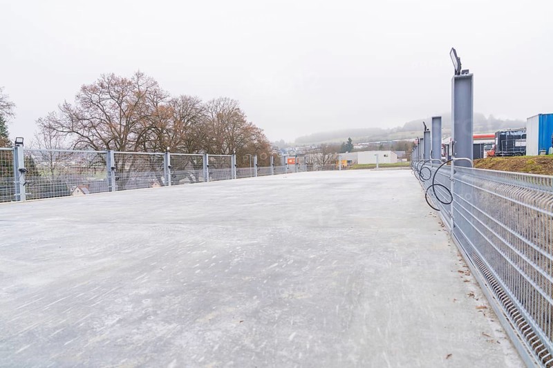 Empty parking lot with mesh fence on a foggy day in an industrial area, parking garage construction with charging infrastructure, Calw, Germany