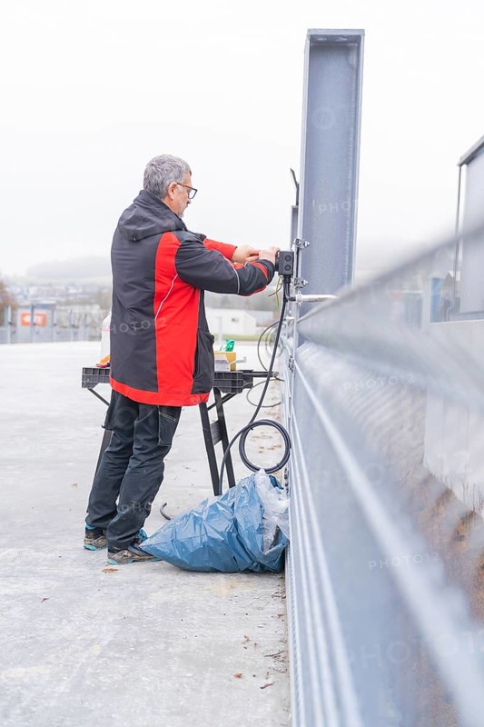 Man working on electrical cable installation in open area, parking garage construction with charging infrastructure, Calw, Germany