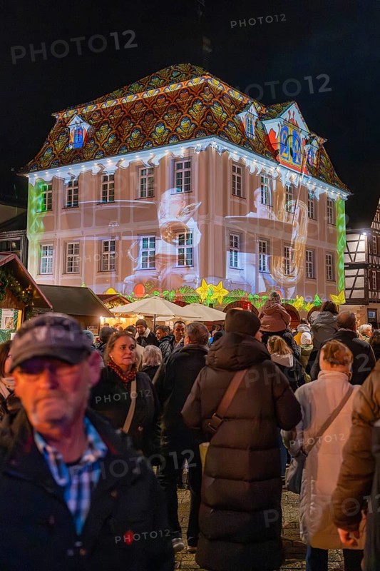 People in a festive square at night with an artistic light show on a building, Weihnachtsmark Nagold, LandkreisCalw, Germany