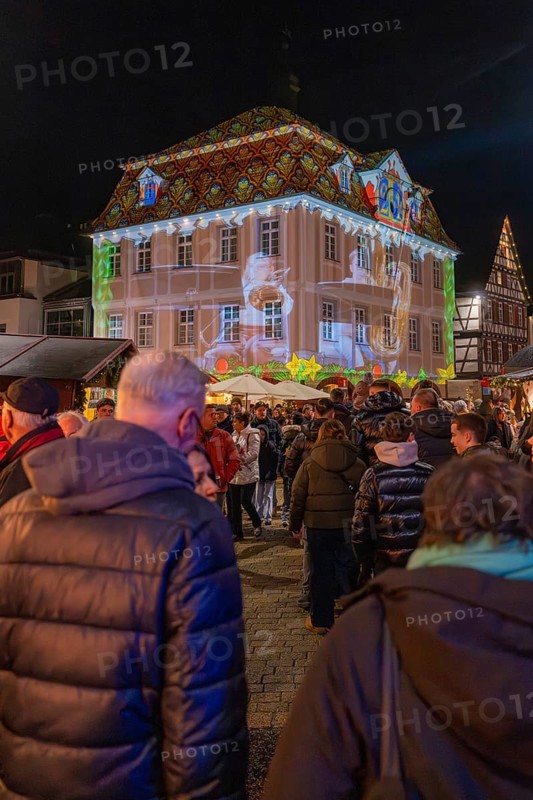 People at a Christmas market in front of an illuminated historic building with a projection, Weihnachtsmark Nagold, LandkreisCalw, Germany