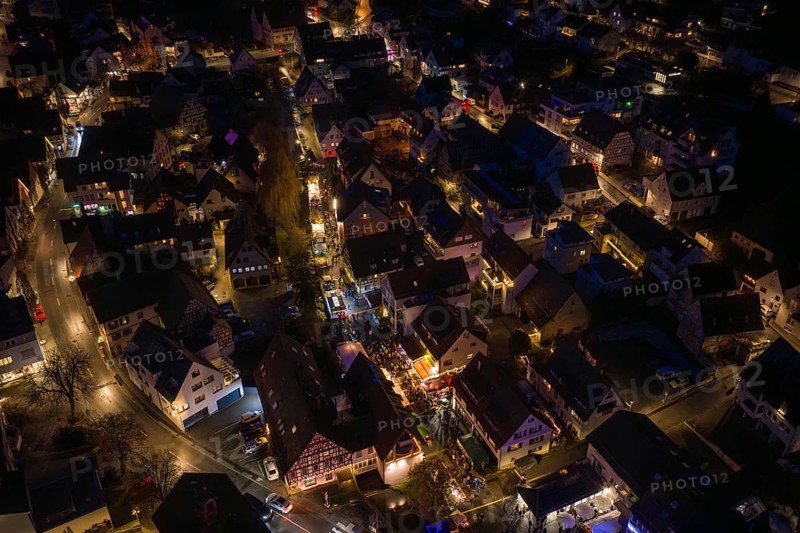 Drone image of an illuminated city at night with visible streets and alleys, Christmas market, Aidingen, Germany