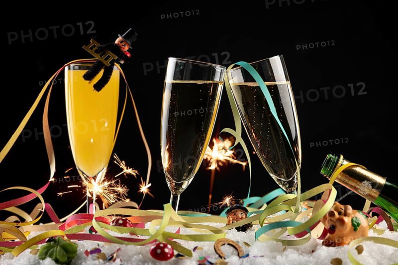 Three champagne glasses with lucky New Year's Day charms, streamers and sparklers in the snow