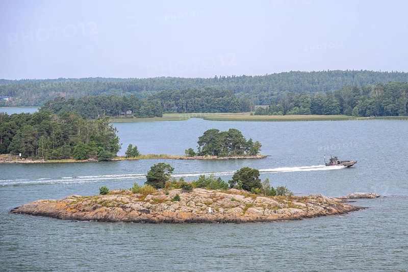 Small, wooded island in calm water with passing patrol boat boat, marine speedboat, Aaland Islands, Finland