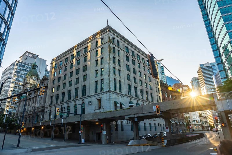 Sun is rising behind waterfront station, casting warm glow on historic building and modern skyscrapers in vibrant downtown vancouver, british columbia
