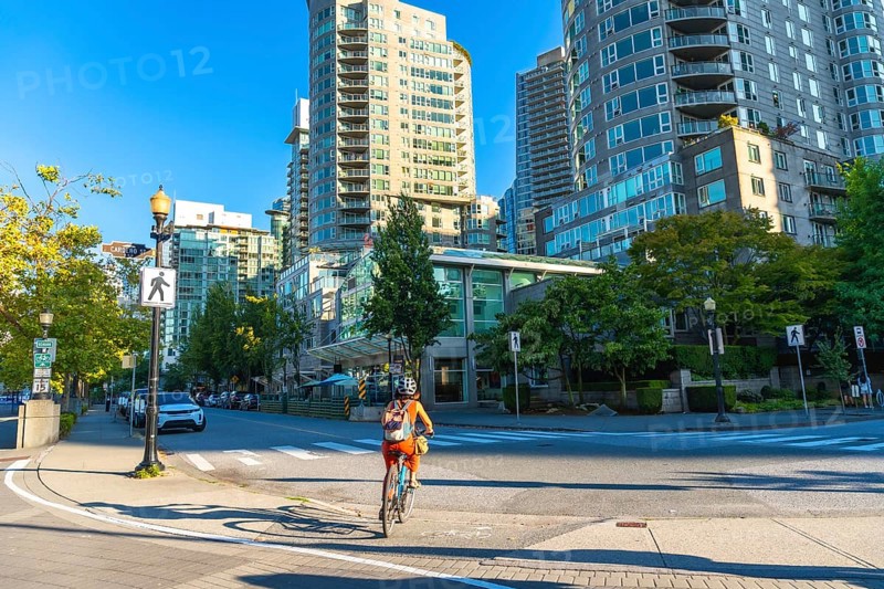 Cyclist enjoying a sunny day, riding a bicycle on a dedicated bike lane in the city center of vancouver, surrounded by modern residential buildings and green trees
