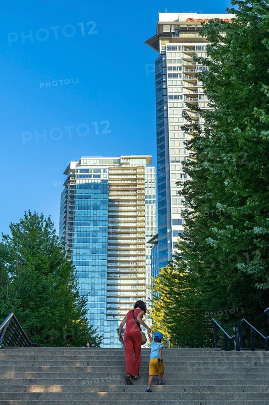 Mother and son climbing stairs together, surrounded by towering skyscrapers and lush trees in downtown vancouver, british columbia, enjoying a sunny summer day in the vibrant city