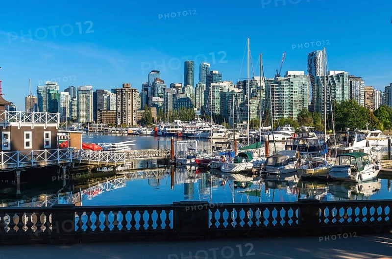 Modern buildings of vancouver reflecting in the calm waters of coal harbour, with yachts and sailboats moored at the marina on a beautiful sunny day in british columbia, canada