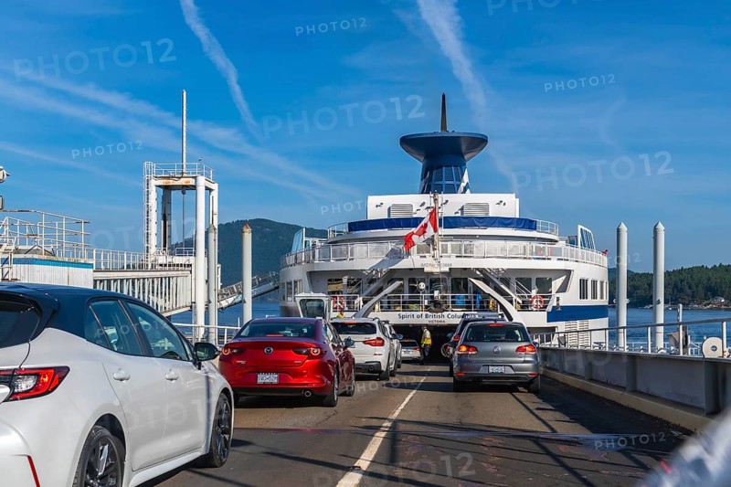 Cars are boarding a ferry with a canadian flag, departing from victoria on vancouver island to vancouver, british columbia, on a sunny day with blue skies