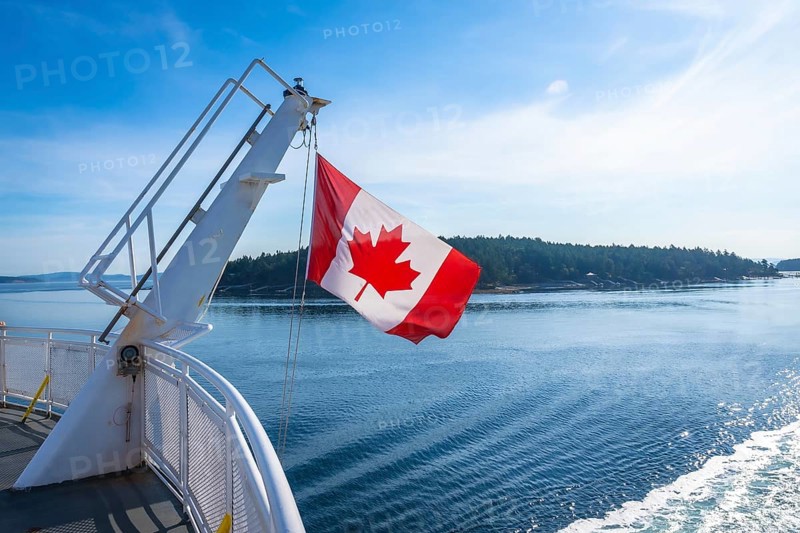The canadian flag waves proudly from a ferry traveling between victoria on vancouver island and vancouver on the mainland of british columbia, showcasing the beauty of the pacific northwest