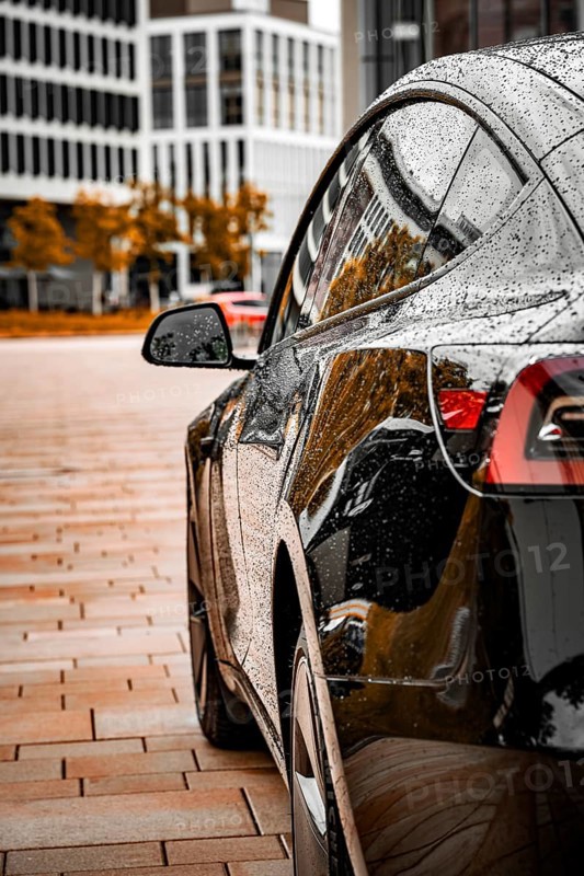 Side view of a wet black car with city in the background, Deer e-car sharing, Tesla Model 3, Calw, Germany
