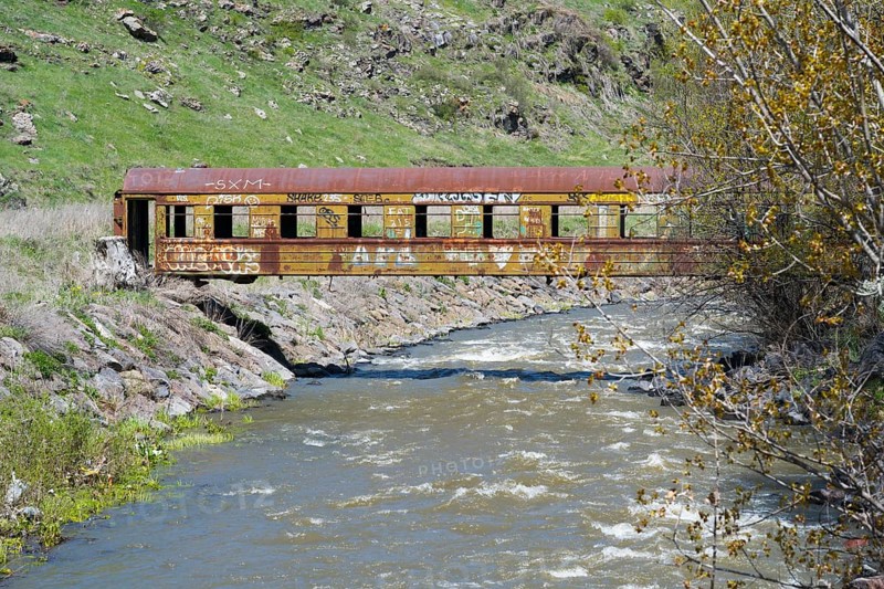 A rusted train car with graffiti stands over a flowing river in a green, hilly landscape, discarded railroad car used as a footbridge, Paravani river, Akhalkalaki, Akhalkalaki, Samtske-Javakheti region, Samtske Javacheti, Lesser Caucasus, Georgia