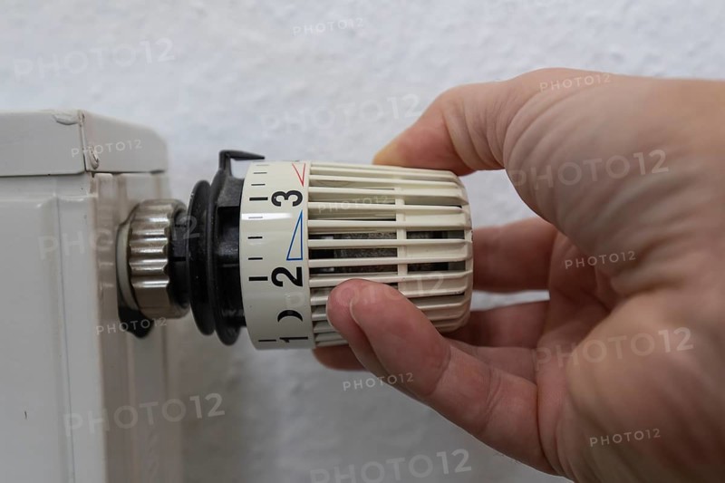 A hand grabs the thermostat head of a radiator to adjust the temperature. This image symbolizes control over the indoor climate and comfort in a modern home. The scene conveys a sense of functionality and homely comfort