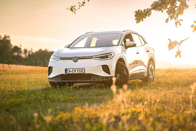 White car standing in a field in warm sunlight at sunset surrounded by grass, VW ID4 electric car, deer car sharing, Calw, Germany
