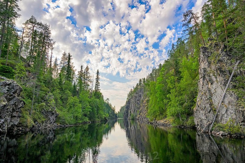 A calm lake lies in a wooded gorge, surrounded by tall rocks and reflecting the sky covered with clouds Julma-Ölkky Canyon Gorge, Hossa National Park, Irni, Northern Ostrobothnia, Finland