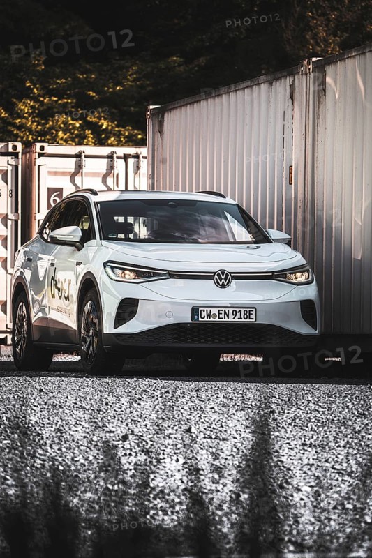 A car on a gravel field next to stacked containers in the shade, VW ID4 electric car, Deer Carsharing, Calw, Germany
