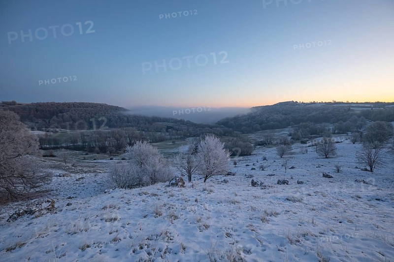 An impressive winter landscape on Randecker Maar near Ochsenwang, where a mystical sea of fog covers the surrounding area. The freezing cold of the morning is reinforced by the snow-covered hills and the soft light. This scene conveys a peaceful, enchanted atmosphere and shows the quiet beauty of nature in winter